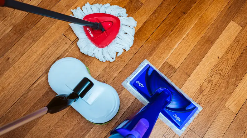 Three different kinds of mops sitting on the floor.