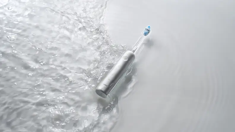 A sleek electric toothbrush lies partially submerged in rippling water, highlighting its water-resistant design against a clean, minimal background.