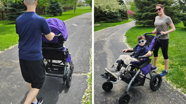 Two adults pushing a small child outdoors, as he sits inside of the Convaid Coaster stroller.