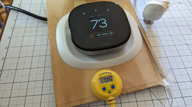 A thermostat is mounted on a board with a thermometer showing 73.4°F.