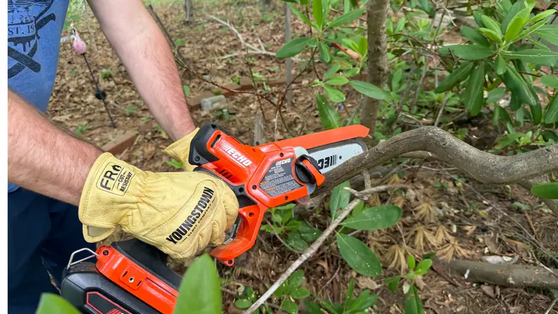 A person cuts through a branch with a small chainsaw