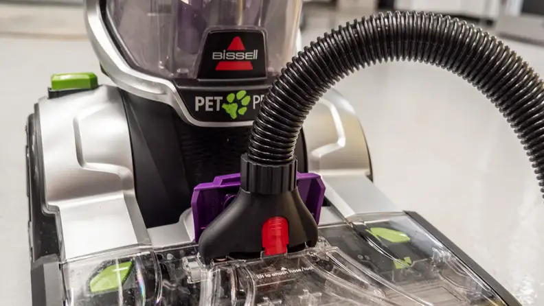 A hose is plugged into the front of a carpet cleaner
