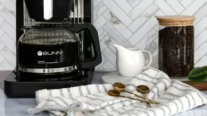 Bunn coffee maker with a full carafe beside a creamer and a jar of coffee beans