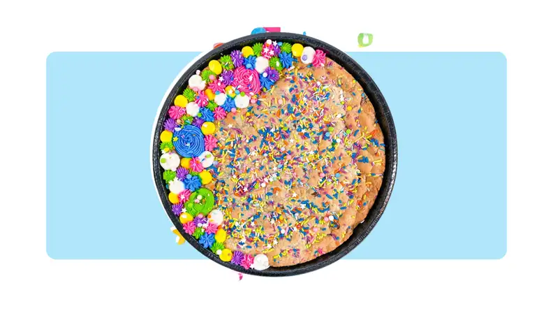 A cookie cake with colored sprinkles, confetti and frosting in front of a background.