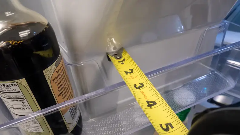 A shot of one of the door bins on the Samsung RF27T5201SG French door refrigerator with measuring tape stretched across its top. The measuring tape shows the bin is only about 2.5" deep.