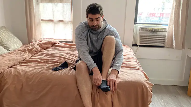 Man sitting on Ziwi bed with peach comforter putting on socks.