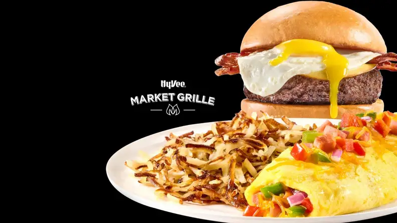 A Hy-Vee Market Grille burger with a fried egg, next to hash browns and an omelet
