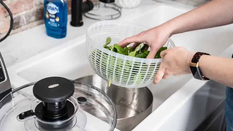 A person rinses salad under a kitchen faucet