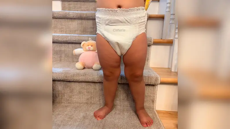 Baby girl standing in front of beige carpeted stairs wearing Coterie The 360 training underwear showing the logo.