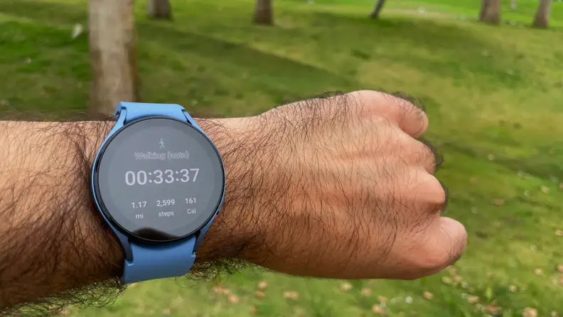 A powered-on smart watch with a light blue wristband wrapped around a person's wrist
