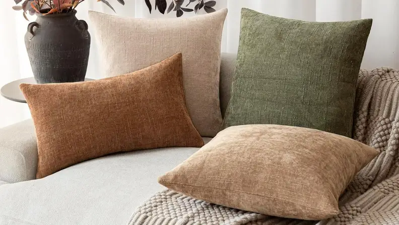 Four throw pillows of various colors, orange, tan, cream, and green, sit on a couch