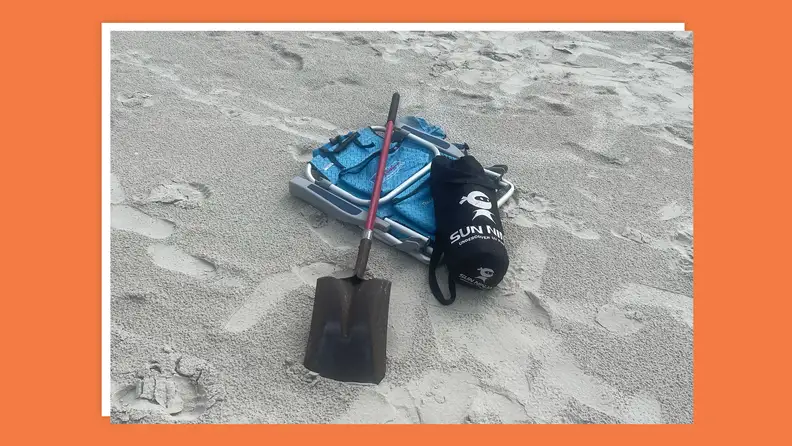 Tent, shovel and beach chair sit together on sandy beach.