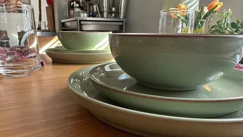 A stack of Denby Pottery plates and glasses on a dinner table.