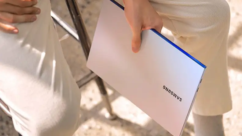 Person holding folded white laptop in hand.