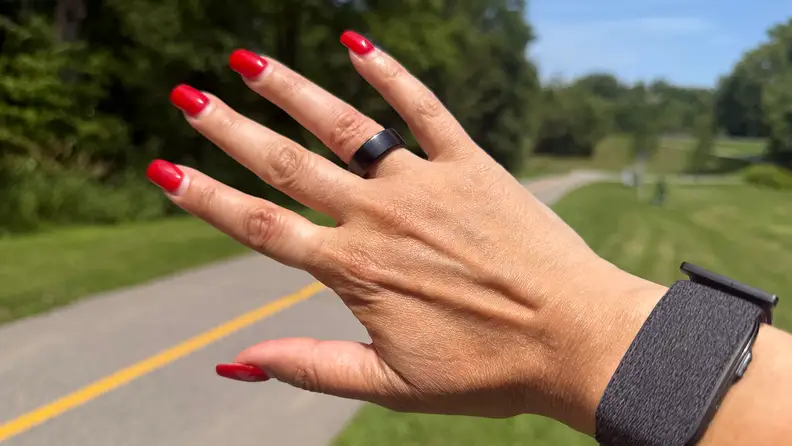 Right hand showing the Pin Pulse Smart Ring in front of a road with green grass behind it.