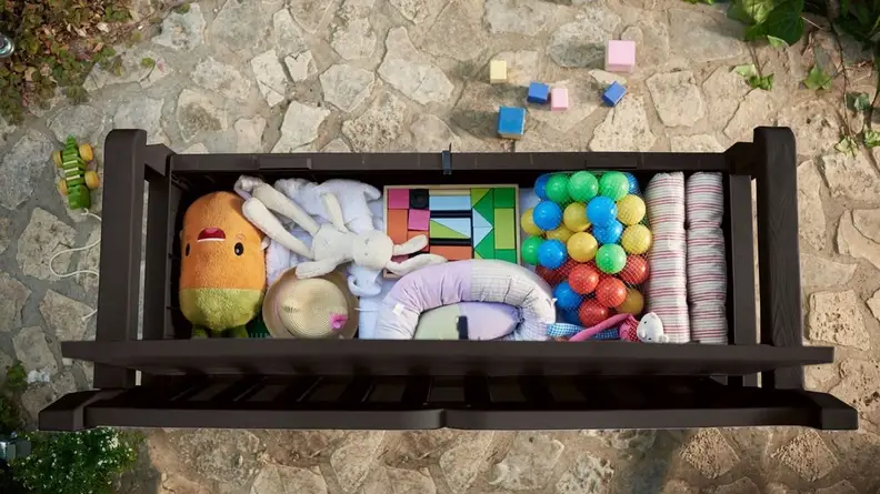 An outdoor wooden bench is shown from above. The seat is lifted up, and a bunch of children's toys are stored neatly inside.