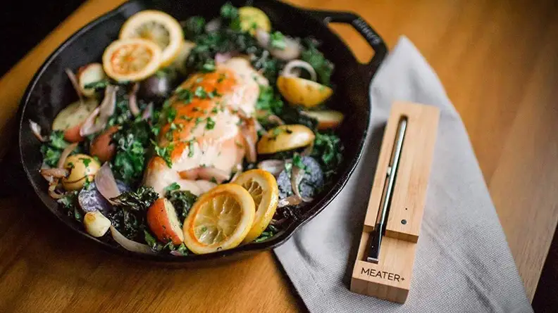A fish dish in a cast iron pan beside the Meater Plus thermometer.