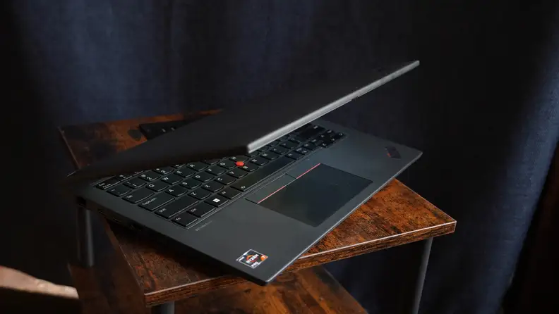 Semi-closed Lenovo ThinkPad P14s Gen 4 laptop in front of navy blue curtain.