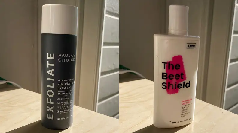Left: Paula's Choice liquid exfoliant sits on a table in a large black bottle. Right: The Beet Shield Antioxidant Day Fluid comes in a white bottle with a splash of pink behind the logo.