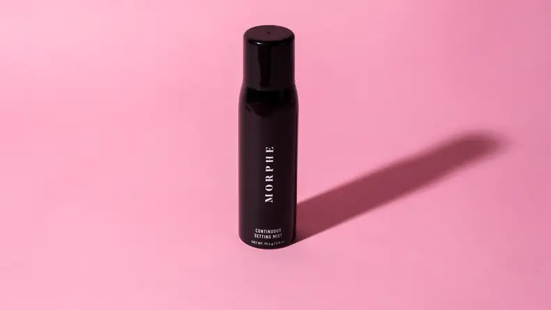 A black bottle of makeup setting spray on a pink background.