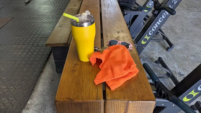 A large insulated tumbler and a gym towel on a bench