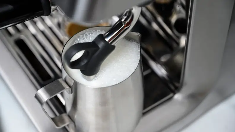 The steaming wand on Breville Infuser in a mug of milk, shot from above.