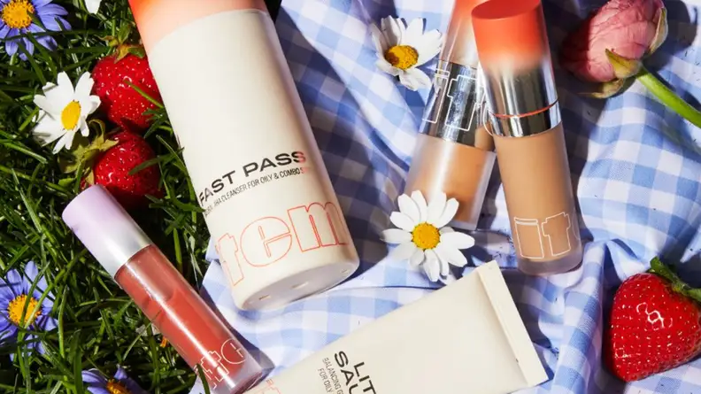 A smattering of Item Beauty products laying on a blue and white checkered blanket.