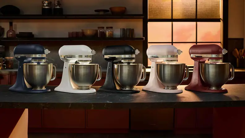 Five KitchenAid Artisan stand mixers in assorted colors displayed on a kitchen countertop.