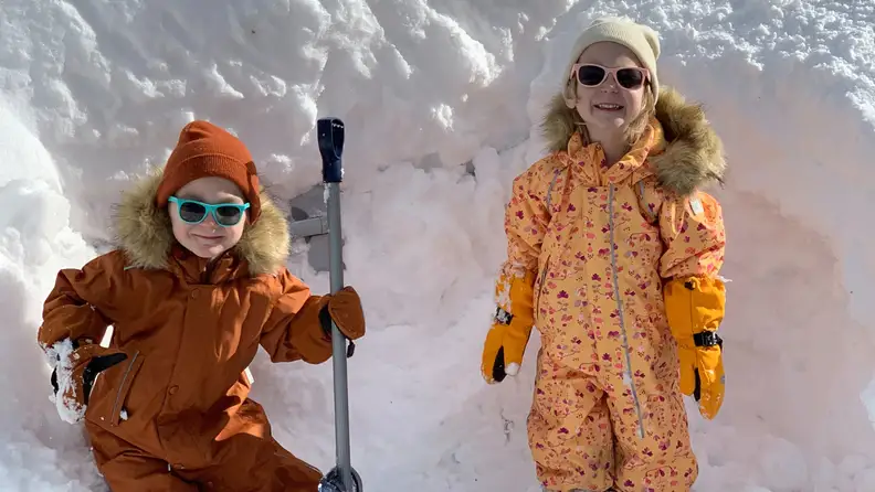 Two children wearing the snowsuit posing in front of snow.