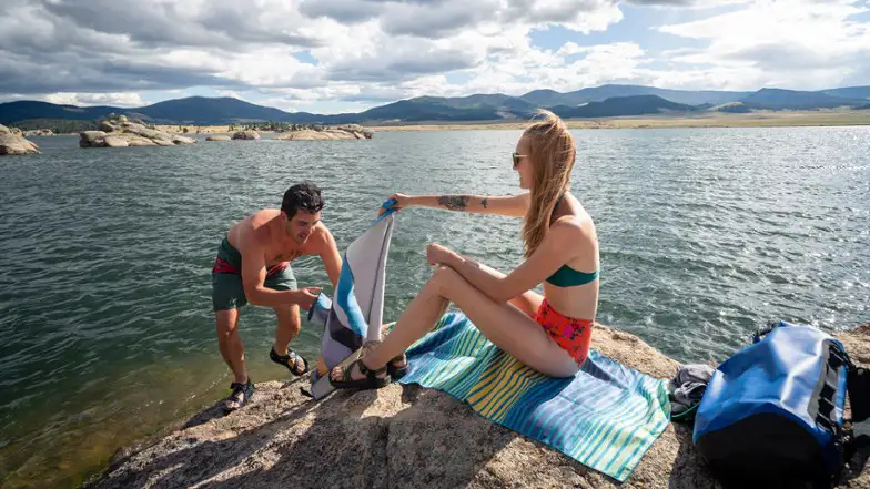 Two people sitting on a towel by a lake.