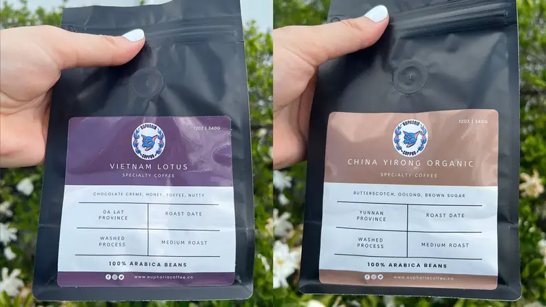 A hand holding up two coffee bean bags