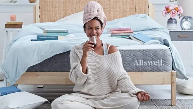 Person smiling on bedroom floor with wine glass in hand.