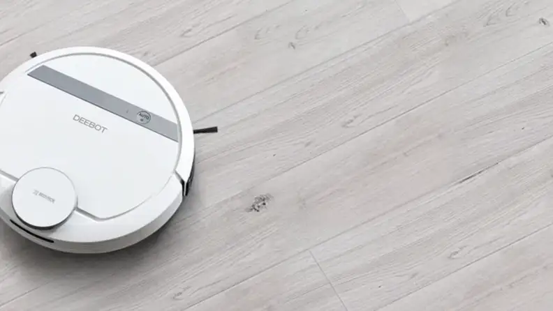 A white robot vacuum in the corner on a gray floor