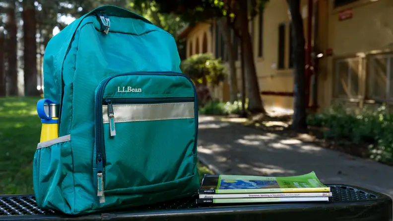 A teal green L.L. Bean backpack on a bench.