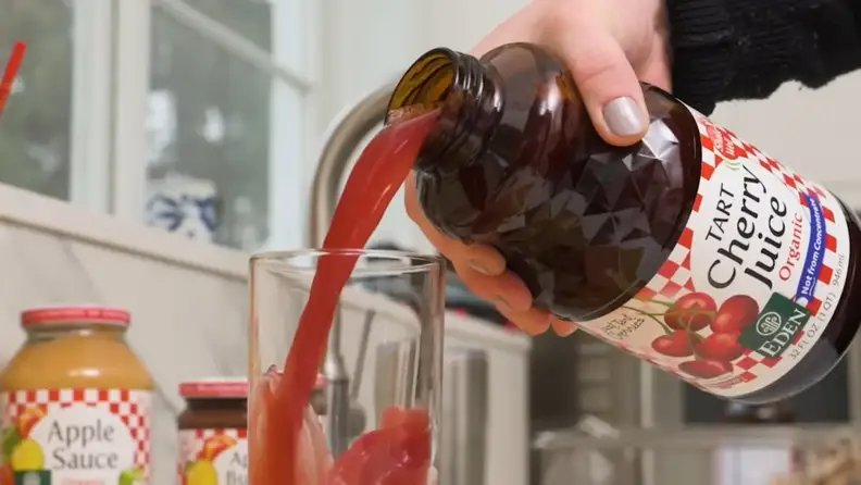 Pouring Eden tart cherry juice into a glass beside applesauce jars