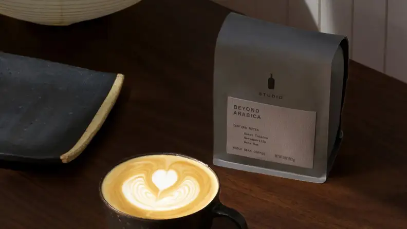 Coffee bag beside a latte with heart-shaped foam art