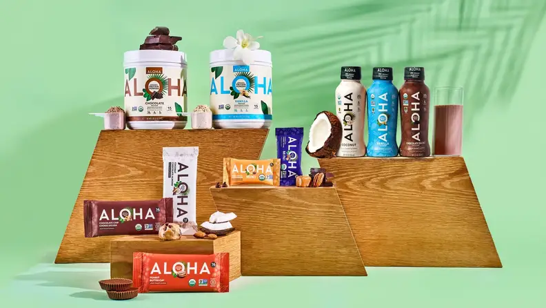 ALOHA protein powders, bars, and drinks displayed on wood risers