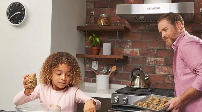 A father and daughter bake cookies together in the kitchen with the Echo Wall Clock in the background.