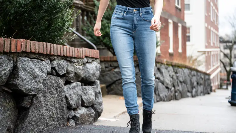 A woman walking down the street in a black shirt and Good American skinny jeans