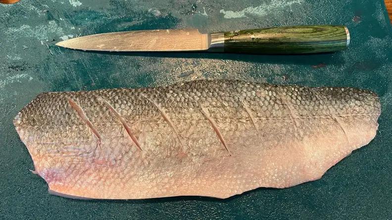 Small, narrow utility knife next to raw fish on countertop surface. filet