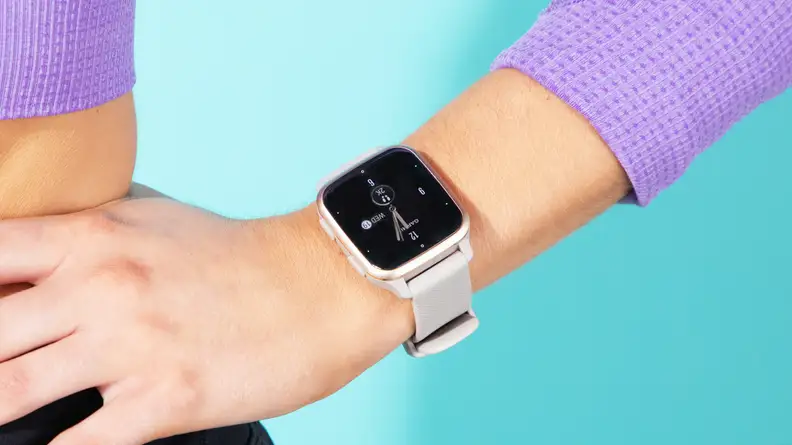 A person rests their hand on their hip while wearing a Garmin Venu Sq 2 fitness tracker.