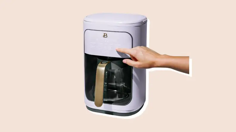 Person using finger to power on lavender-colored coffee maker from the Beautiful by Drew Barrymore Kitchen Appliances line.