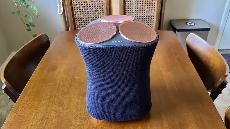 Sony SRS-RA5000 hour-glass shaped speaker sits on a wooden table with its black fabric front and copper tops showing