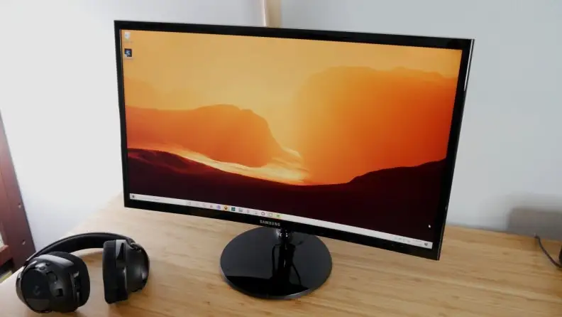 The Samsung C24F390computer monitor and a pair of headphones on a office desk.