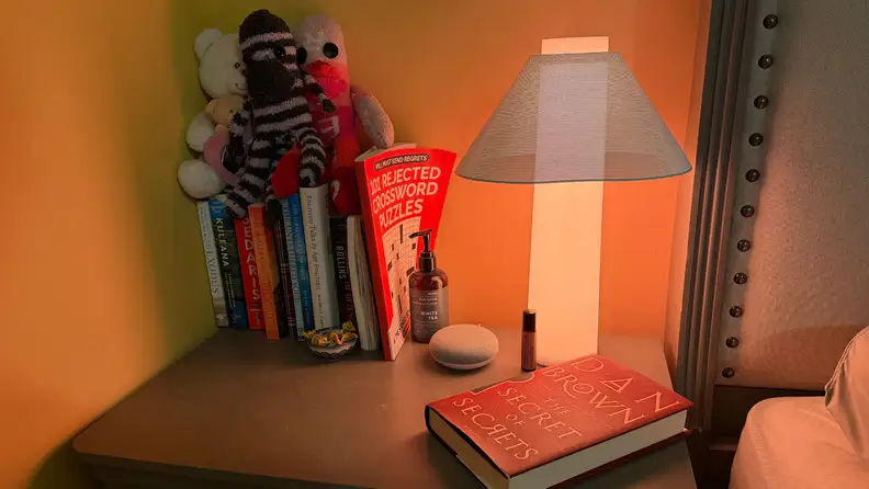 Loftie lamp on a nightstand next to a set of books with stuffed animals on top.