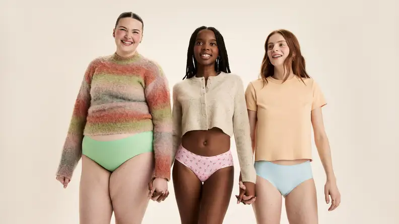 Three teens of diverse body types smiling and holding hands while modeling comfortable period underwear.