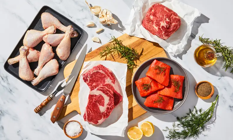 Raw poultry, beef, pork, and salmon on marble countertop.