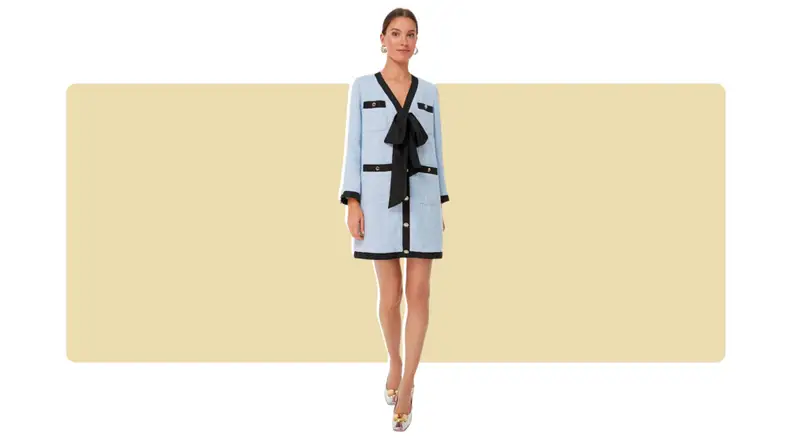 A light blue tweed dress with black piping, gold buttons, and a loose black bow at the center.