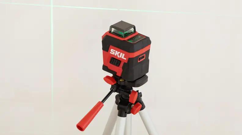 A red laser level on a tripod shoots a green laser onto a wall.