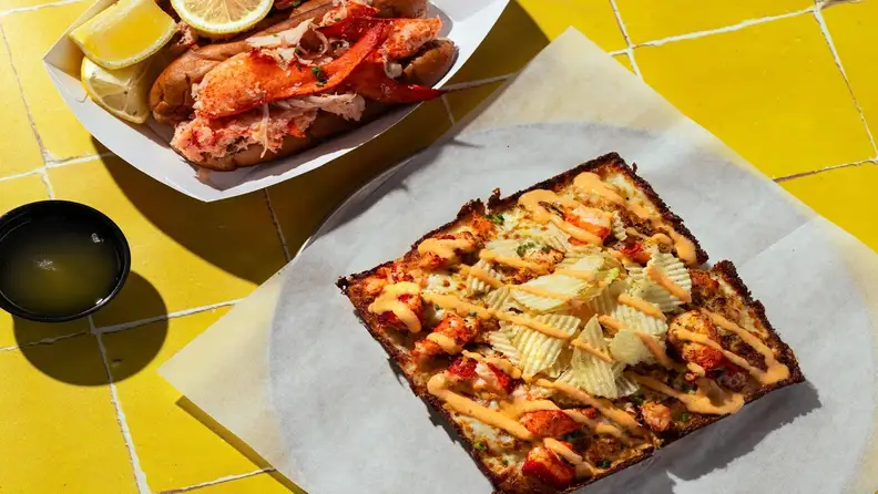 A lobster roll next to a square slice of lobster pizza with chips and drizzle